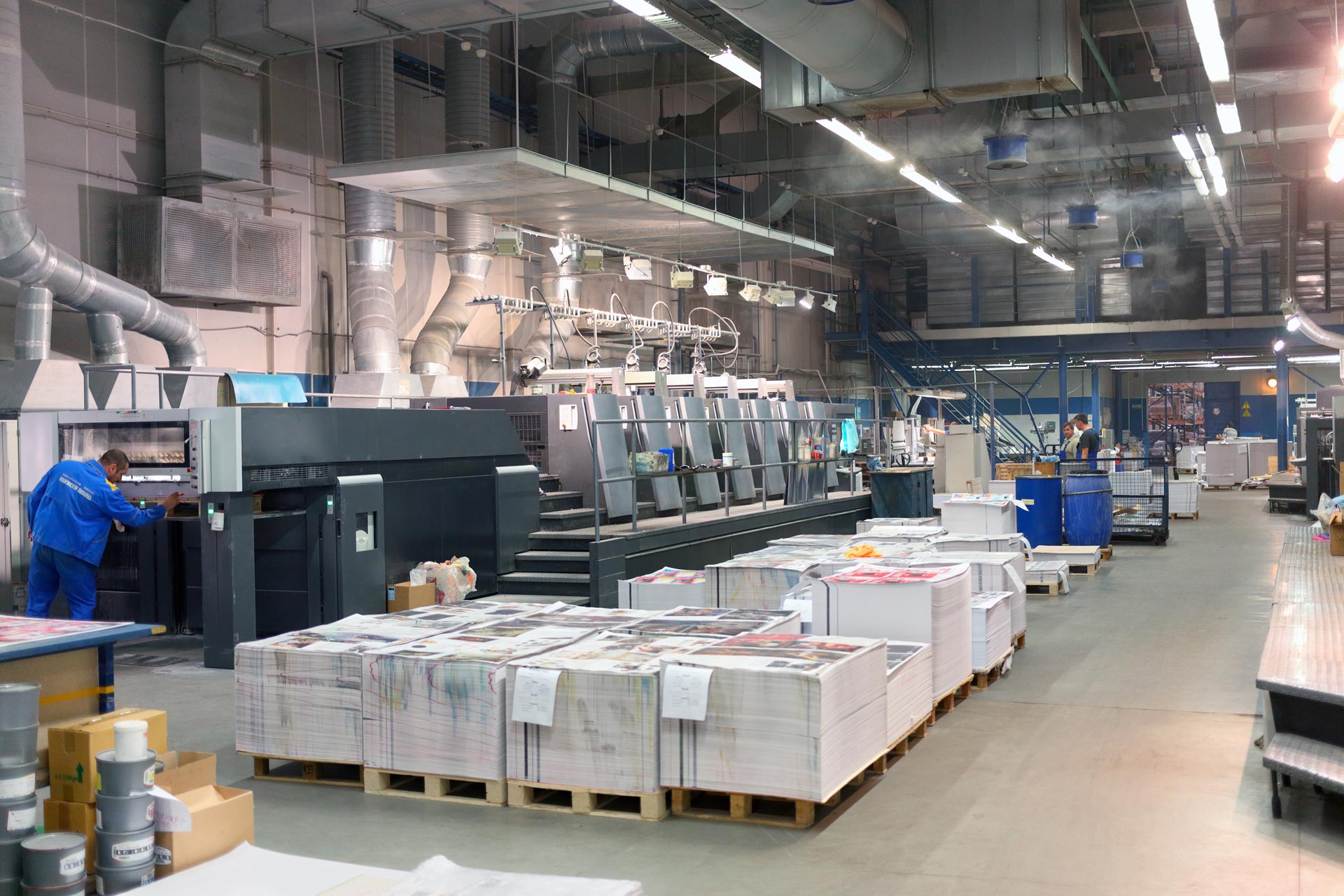 Photo d'une imprimerie. On peut apercevoir des papiers, des machines et trois personnes.